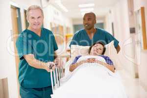 Two Orderlies Pushing A Woman In A Bed Down A Hospital Corridor
