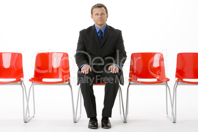 Businessman Sitting In Row Of Empty Chairs