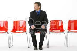 Businessman Sitting In Row Of Empty Chairs