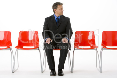 Businessman Sitting In Row Of Empty Chairs