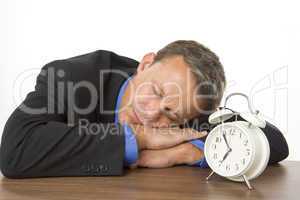 Businessman Asleep On Desk By An Alarm Clock