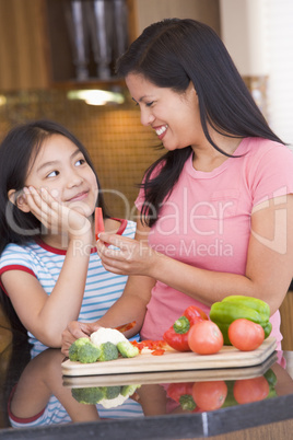 Mother Offering Daughter A Piece Of Freshly Chopped Pepper