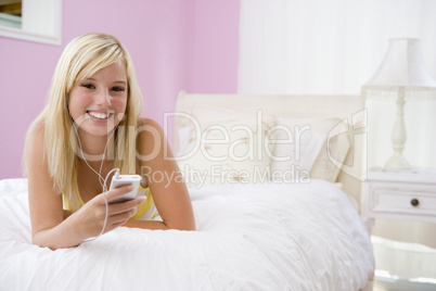 Teenage Girl Lying On Bed Using Mp3 Player