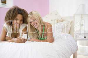 Teenage Girls Lying On Bed Listening To Mp3 Player