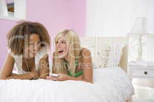 Teenage Girls Lying On Bed Listening To Mp3 Player