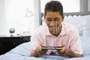 Teenage Boy Lying On Bed Playing Video Game