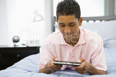 Teenage Boy Lying On Bed Playing Video Game