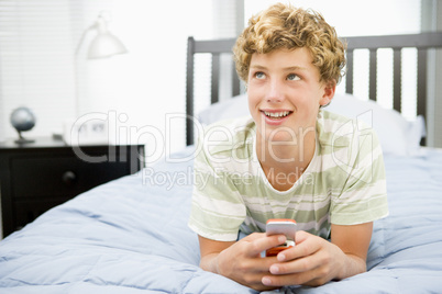 Teenage Boy Lying On Bed Using Mobile Phone