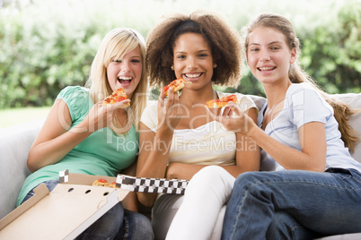 Teenage Girls Sitting On Couch And Eating Pizza Together