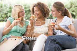 Teenage Girls Sitting On Couch And Eating Pizza Together