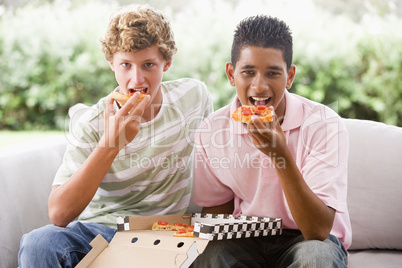 Teenage Boys Sitting On Couch Eating Pizza Together