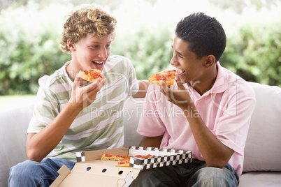 Zwei Jungen essen gemeinsam Pizza auf dem Sofa