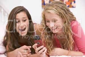 Teenage Girls Lying On Bed Using Mobile Phone