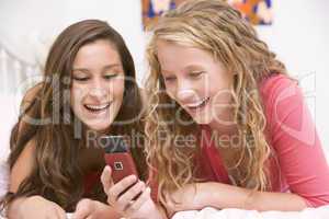 Teenage Girls Lying On Bed Using Mobile Phone