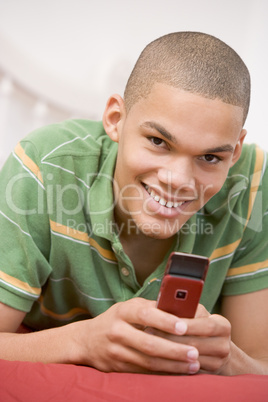 Teenage Boy Lying On Bed Using Mobile Phone