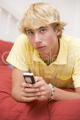 Teenage Boy Lying On Bed Using Mobile Phone