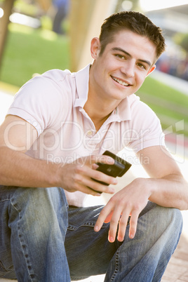 Teenage Boy Sitting Outdoors Using Mobile Phone