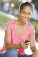 Teenage Girl Sitting Outdoors Using Mobile Phone