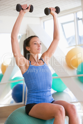 Woman Using Hand Weights On Swiss Ball At Gym