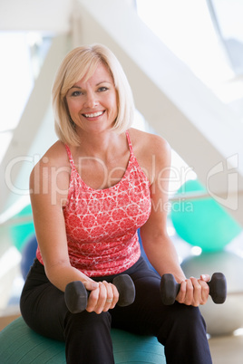 Woman Using Hand Weights On Swiss Ball At Gym