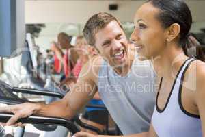 Personal Trainer Encouraging Woman Using Treadmill At Gym