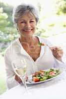 Ältere Frau isst von einem Salatteller mit Fleischbeilage