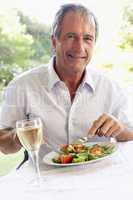 Mann sitzt vor einem Salatteller bei einem Glas Wein