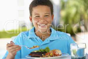 Junge sitzt vor einem Teller mit Fleisch und Salat