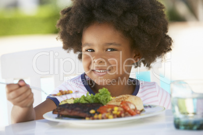 Süßes Kind mit dunkler Haut sitzt vor einem Teller