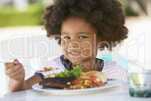 Süßes Kind mit dunkler Haut sitzt vor einem Teller