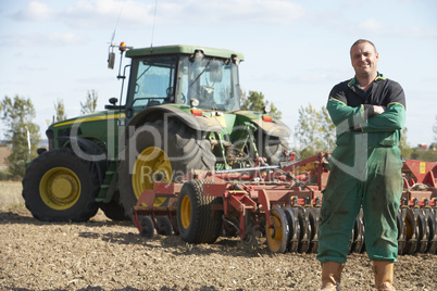 Ein Bauer steht mit verschränkten Armen vor einem Traktor