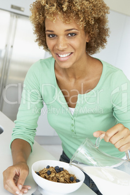 Eine Frau gießt sich Milch über Schale CornFlakes