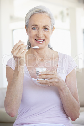 Frau mit grauen Haaren isst einen Naturjoghurt