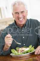 Ein Mann mit grauem Haar sitzt vor einem Salatteller