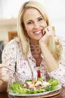 Blonde Frau sitzt am Tisch und ist einen Teller Salat