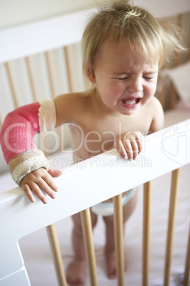 Kleinkind steht weinend im Gitterbett