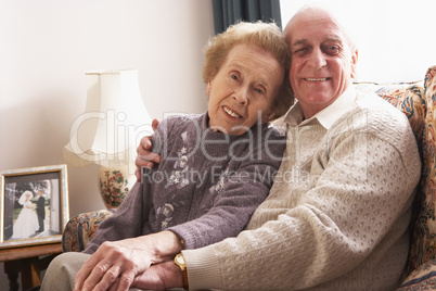 Älteres Ehepaar sitzt eng umarmt im Wohnzimmer