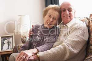 Älteres Ehepaar sitzt eng umarmt im Wohnzimmer