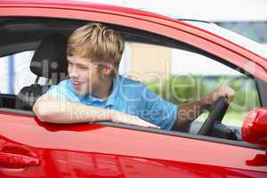 Junger Mann sitzt in einem roten Auto und lacht