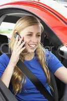 Junge blonde Frau sitzt im roten Auto und telefoniert