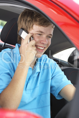 Junger Mann sitzt im roten Auto und telefoniert