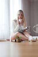 young blond woman sits with a cup of coffee on the floor