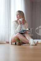 young blond woman sits with a cup of coffee on the floor