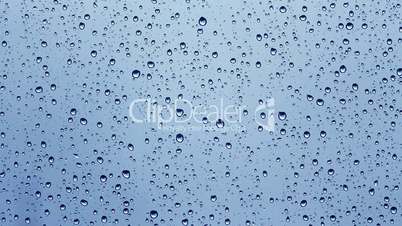 Time lapse of rain water drops on the window glass on blue background