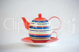 A teapot with stripes on a matching cup and saucer.