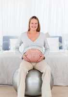 Pretty future mother sitting on a fitness ball and touching her