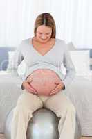 Cute pregnant woman touching her belly sitting on a fitness ball