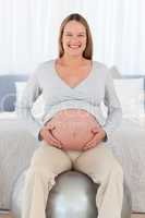 Front view of a happy future mom sitting on a fitness ball