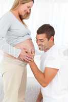 Happy man in knee feeling the belly of his pregnant wife