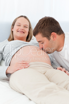 Lovely man kissing the belly of his pregnant wife in the bed